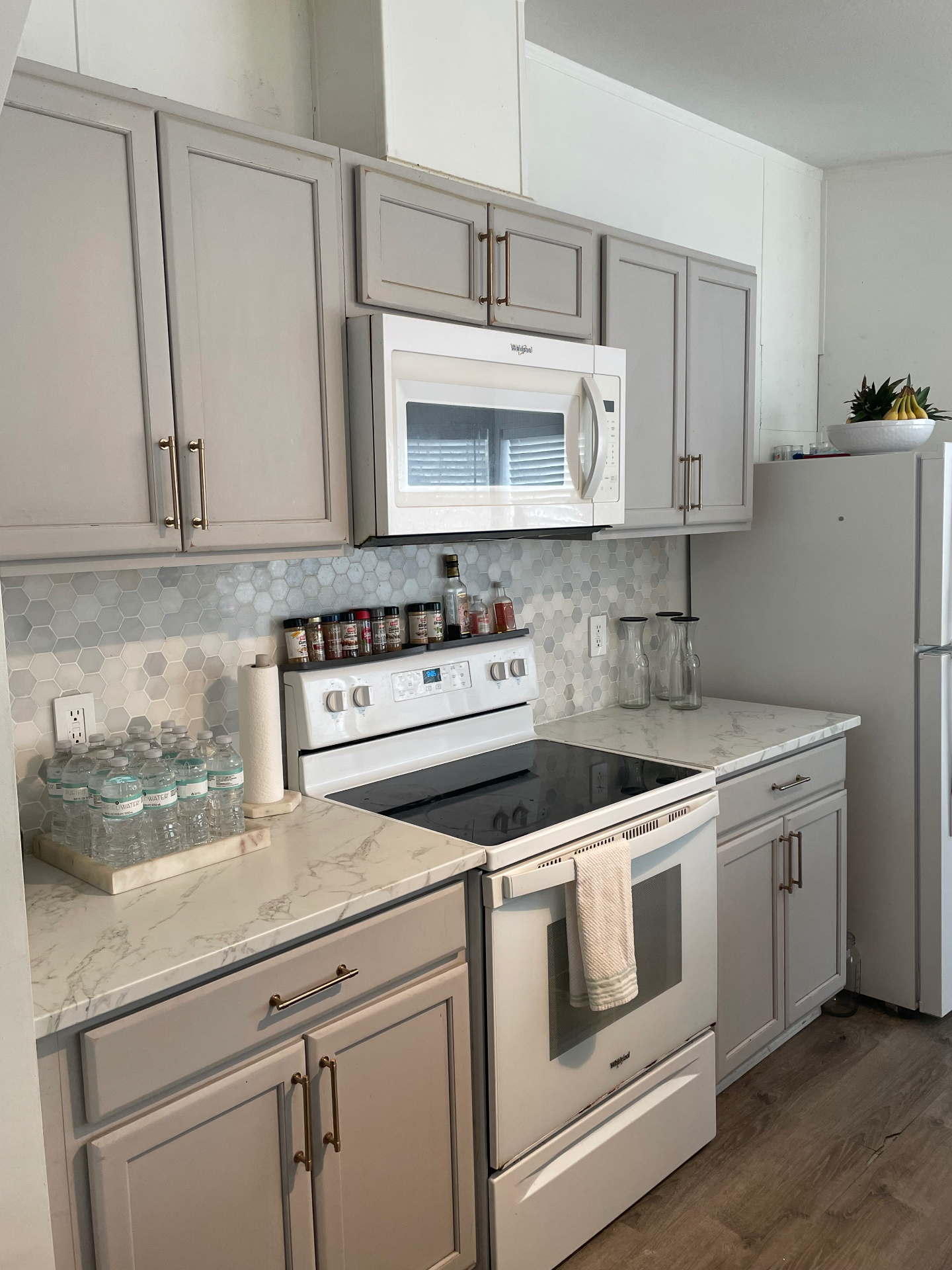 Kitchen with grey shaker cabinets, marble backsplash and brass hardware
